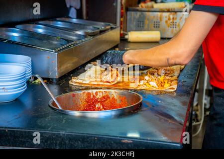 Cibo di strada turco. L'uomo cuoce la tradizionale torta di grigliate nella città vecchia di Antalya, Turchia Foto Stock