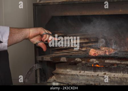 Lo chef prepara bistecche di manzo al fuoco aperto nel ristorante Foto Stock