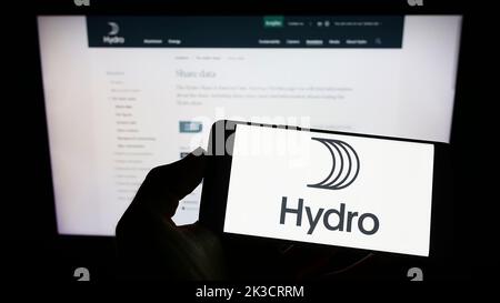 Persona che tiene uno smartphone con il logo della società norvegese di alluminio Norsk Hydro ASA sullo schermo di fronte al sito Web. Messa a fuoco sul display del telefono. Foto Stock