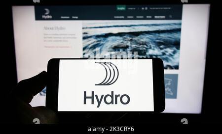 Persona che tiene il cellulare con il logo della società norvegese di alluminio Norsk Hydro ASA sullo schermo di fronte alla pagina web aziendale. Messa a fuoco sul display del telefono. Foto Stock