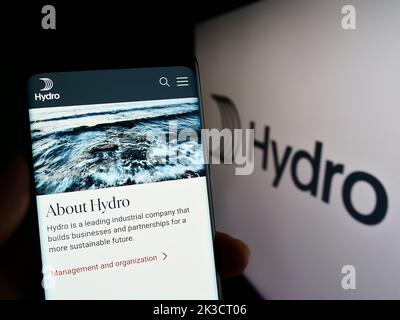 Persona che tiene il telefono cellulare con il sito web della società norvegese di alluminio Norsk Hydro ASA sullo schermo con il logo. Messa a fuoco al centro del display del telefono. Foto Stock