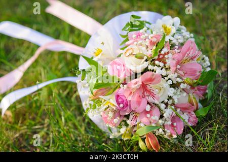 Bouquet nuziale di fiori e anelli d'oro per matrimoni. Bouquet nuziale di rose rosa e bianche adagiate su un prato Foto Stock