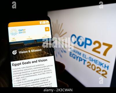 Persona che tiene il cellulare con il sito web di 2022 ONU Climate Change Conference (COP27) sullo schermo di fronte al logo. Messa a fuoco al centro del display del telefono. Foto Stock