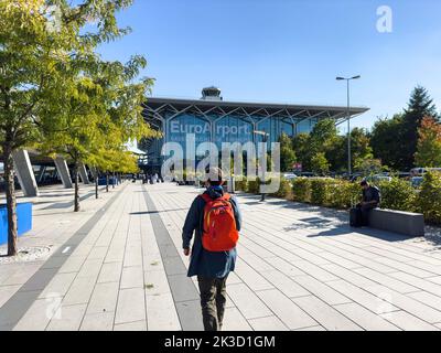 Basilea, Svizzera - 22 settembre 2022: Giovane turista maschio con zaino rosso a piedi verso l'edificio principale di EuroAirport Basilea-Mulhouse-Friburgo hub aeroporto internazionale in Germania Francia e Svizzera Foto Stock