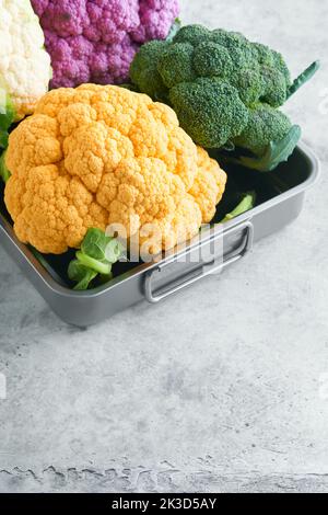 Cavolfiore di Colorfu. Vari tipi di cavolfiore su fondo grigio in cemento. Cavoli di colore viola, giallo, bianco e verde. Broccoli e Romanesco. Foto Stock