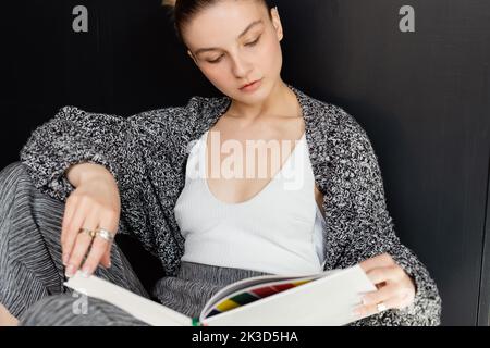 Giovane donna in cardigan lavorato a maglia lettura libro a casa, immagine stock Foto Stock