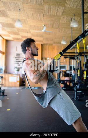 Foto verticale di un uomo forte che fa esercizi con trx in palestra Foto Stock