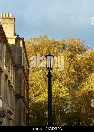 Bagno autunnale - gli emblematici edifici georgiani in pietra da bagno e un vecchio lampione in ferro all'ombra davanti ad un albero di colore autunnale in luce solare Foto Stock