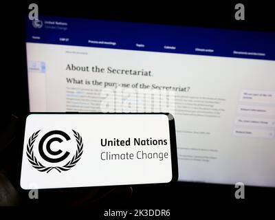 Persona che tiene in mano uno smartphone con il logo del trattato delle Nazioni Unite sull'ambiente UNFCCC sullo schermo di fronte al sito Web. Messa a fuoco sul display del telefono. Foto Stock