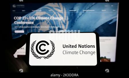 Persona che tiene il telefono cellulare con il logo del trattato ambientale delle Nazioni Unite UNFCCC sullo schermo di fronte alla pagina web. Messa a fuoco sul display del telefono. Foto Stock