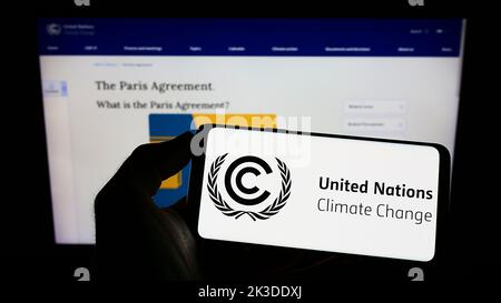 Persona che tiene il cellulare con il logo del trattato ambientale delle Nazioni Unite UNFCCC sullo schermo di fronte alla pagina web. Messa a fuoco sul display del telefono. Foto Stock