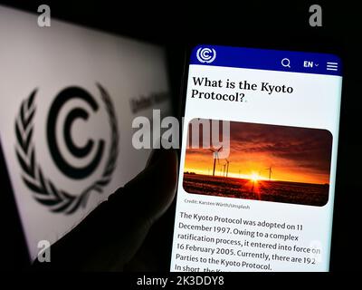 Persona che tiene in mano uno smartphone con il sito Web del trattato ambientale delle Nazioni Unite UNFCCC sullo schermo davanti al logo. Messa a fuoco al centro del display del telefono. Foto Stock