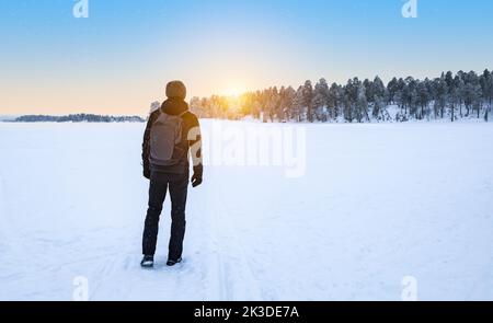 Viaggiatore maschio con zaino a piedi nella neve godendo il tramonto. Lapponia, Finlandia. Foto Stock