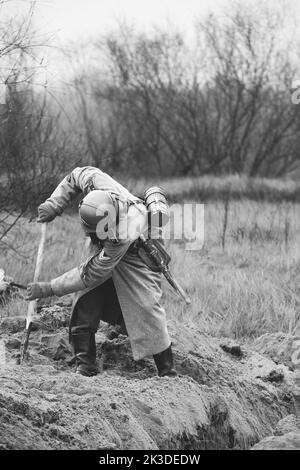 Re-enactor vestito come tedesco Wehrmacht Fanteria Soldato nella seconda guerra mondiale con Shovel scavi trincea. Posizione difensiva. Vestito militare tedesco di tedesco Foto Stock