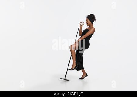 Studio di cantante africana femminile con microfono isolato su sfondo bianco studio. Jazz, soul music, melodia e stile retrò Foto Stock