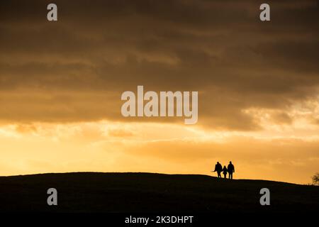 Silhouette di una famiglia di tre persone che camminano nel tramonto su una collina. Foto Stock