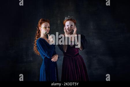 Ritratto di due belle donne a immagine di regine in maschere facciali su sfondo scuro. Cura della pelle Foto Stock