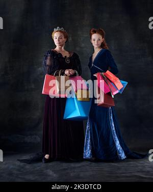 Ritratto di due belle donne a immagine di regine con molti sacchetti di shopping isolato su sfondo scuro Foto Stock