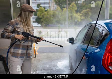 Donna che lava un'auto in una stazione di lavaggio auto self-service con schiuma di wahing. Stazione di lavaggio auto self-service Foto Stock