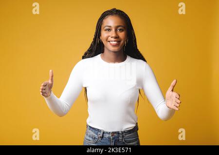 Donna multirazziale che mostra con la lunghezza delle mani, misura simbolo isolato su giallo. Una studentessa manager che si erge e dimostra la dimensione di qualcosa di grande Foto Stock