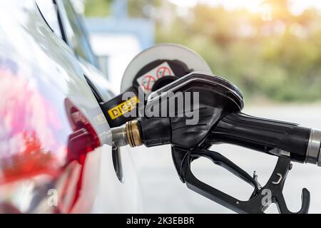 Primo piano dettaglio maniglia a pistola nera inserita nel serbatoio carburante bianco per auto diesel presso la stazione di rifornimento benzina. Manutenzione self-service Foto Stock