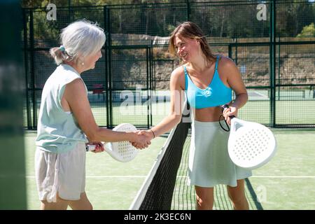 Donne anziane e giovani che si stringono dopo il padel tennis match Foto Stock