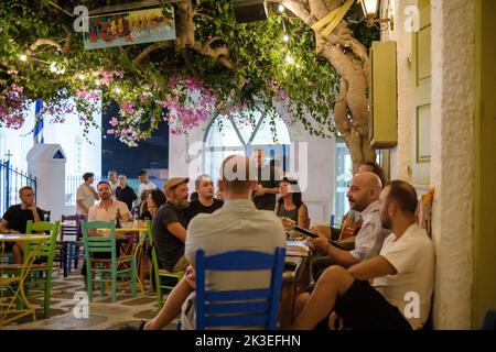 IOS, Grecia - 11 settembre 2022 : pittoresca terrazza all'aperto con sedie colorate e locali che suonano musica tradizionale dal vivo in iOS cicladi Grecia Foto Stock