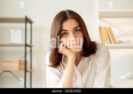 Lezione noiosa. Formazione online. Videoconferenza. Donna non interessata che appoggia la testa sulla mano guardando la fotocamera home workplace sfondo interno. Foto Stock