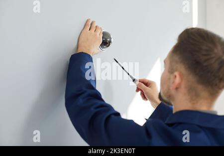 Tecnico che ripara la telecamera dome CCTV di sorveglianza sulla parete all'interno dell'edificio Foto Stock