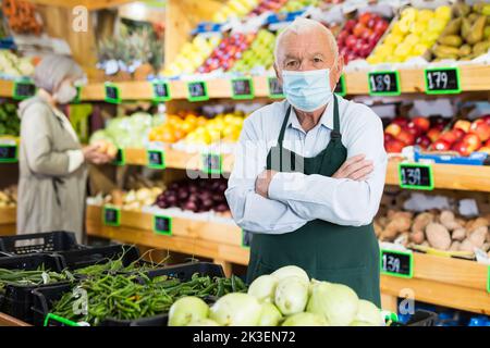 Il dipendente di un supermercato anziano che indossa una maschera protettiva lavora nell'area di vendita Foto Stock