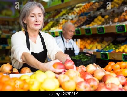 Donna lavoratore supermercato impilare frutta su scaffale in sala di vendita Foto Stock