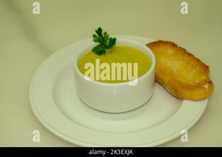 Crema di zucchine con pane tostato, servita in un recipiente bianco Foto Stock