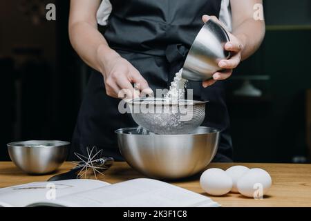 Le giovani mani femminili versano la farina da un piatto in un primo piano del setaccio Foto Stock