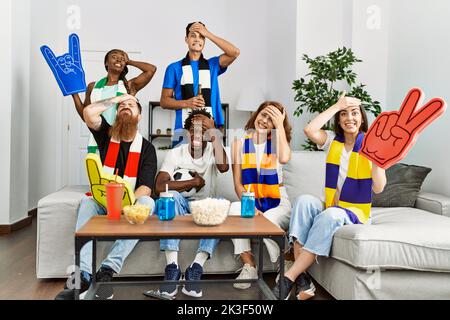 Gruppo di amici che sostengono la squadra di calcio che guarda la tv a casa seduta sul divano stressato e frustrato con mano sulla testa, sorpreso e faccia arrabbiata Foto Stock