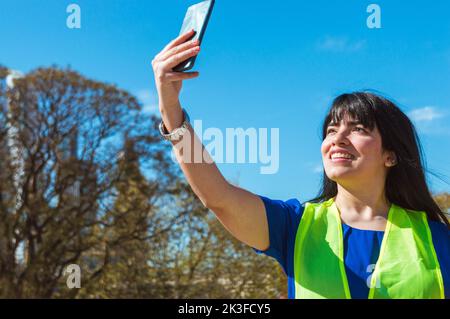 giovane latina venezuelana ingegnere donna al suo lavoro prende un selfie con il suo telefono per inviare al suo ragazzo, tecnologia concetto, copia spazio. Foto Stock