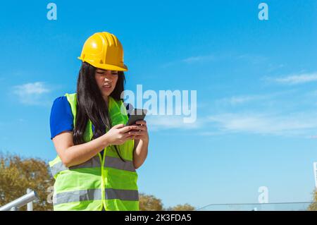 giovane donna venezuelana caucasica latina, ingegnere esterno al lavoro infastidito rispondere al suo capo un messaggio al telefono, chiedendo spiegazioni per cattiva wo Foto Stock