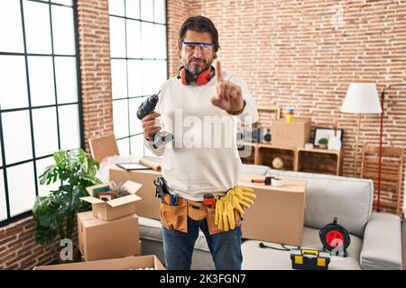 Bell'uomo di mezza età che tiene il cacciavite a casa nuova puntando con il dito verso l'alto e l'espressione arrabbiata, senza mostrare alcun gesto Foto Stock