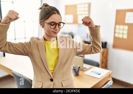 Giovane bruna adolescente che indossa lo stile di lavoro in ufficio mostrando braccia muscoli sorridenti orgogliosi. Concetto di fitness. Foto Stock