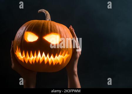 Faccia di zucca con luce di candela all'interno in uno sfondo scuro fumoso, trucco o delizia. Decorazione per feste di Halloween. Simbolo spaventoso espressione Jack-o-lantern attivata Foto Stock