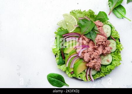 Insalata di tonno con avocado, cetriolo, cipolla rossa e lattuga. Sfondo in pietra bianca, vista dall'alto, spazio copia Foto Stock