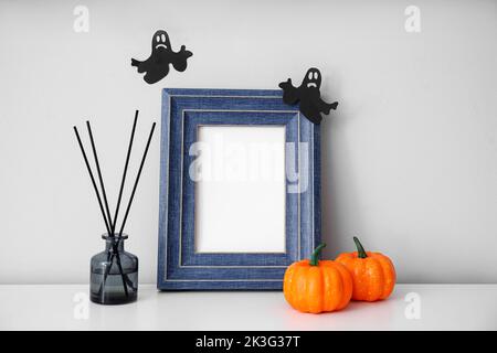 Cornice fotografica vuota con zucche di Halloween e diffusore a lamelle sulla lampada accanto alla parete Foto Stock