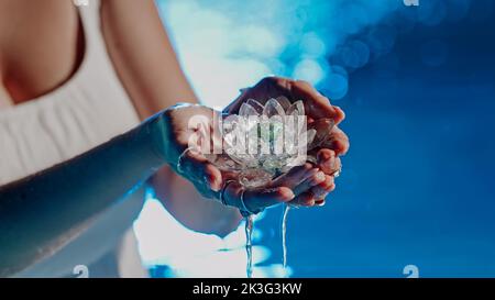 Donna che tiene fragile fiore di loto. Gocce d'acqua pulite gocciolano dal cristallo. Concetto di religione, kundalini, meditazione, chakra, interiore spirituale Foto Stock