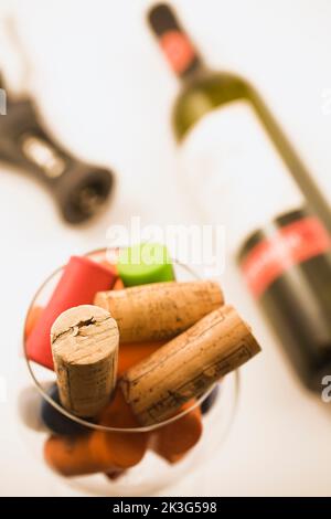 Bicchiere di vino riempito con tappi di sughero e bottiglia di vino vuota e cavatappi su sfondo bianco. Foto Stock