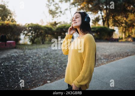 Ragazza adolescente che sente la musica. Utilizza le cuffie per riprodurre musica sul suo smartphone nel parco. Foto Stock