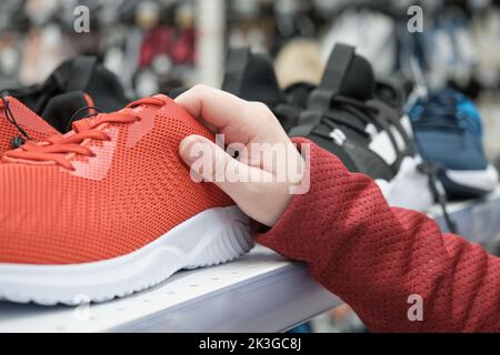 Donna in un negozio di scarpe sceglie di acquistare, rosso sport sneakers in una maglia per camminare Foto Stock