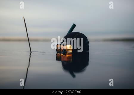 Pescatore subacqueo alla ricerca di pesci in mezzo al mare al tramonto. Pescatore che tiene il suo fucile mentre sommerso in acqua di mare. Foto Stock