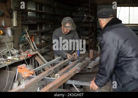 La saldatrice trattiene il metallo. Persone in officina metallo. Lavori in garage. Operatore nella maschera protettiva. Foto Stock