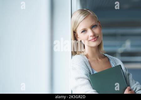 Mettere la sua istruzione al primo posto. Una giovane studentessa pensierosa nel corridoio con i suoi libri. Foto Stock