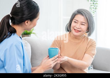 Donna che si prende cura di servire la sua paziente anziana soddisfatto con una tazza di caffè a casa, sorridendo l'uno con l'altro. Assistenza medica per pensionati, Salute domestica Foto Stock