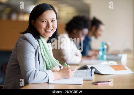 Cramming alcune conoscenze dell'ultimo minuto. Una giovane donna che studia in biblioteca con altri studenti. Foto Stock